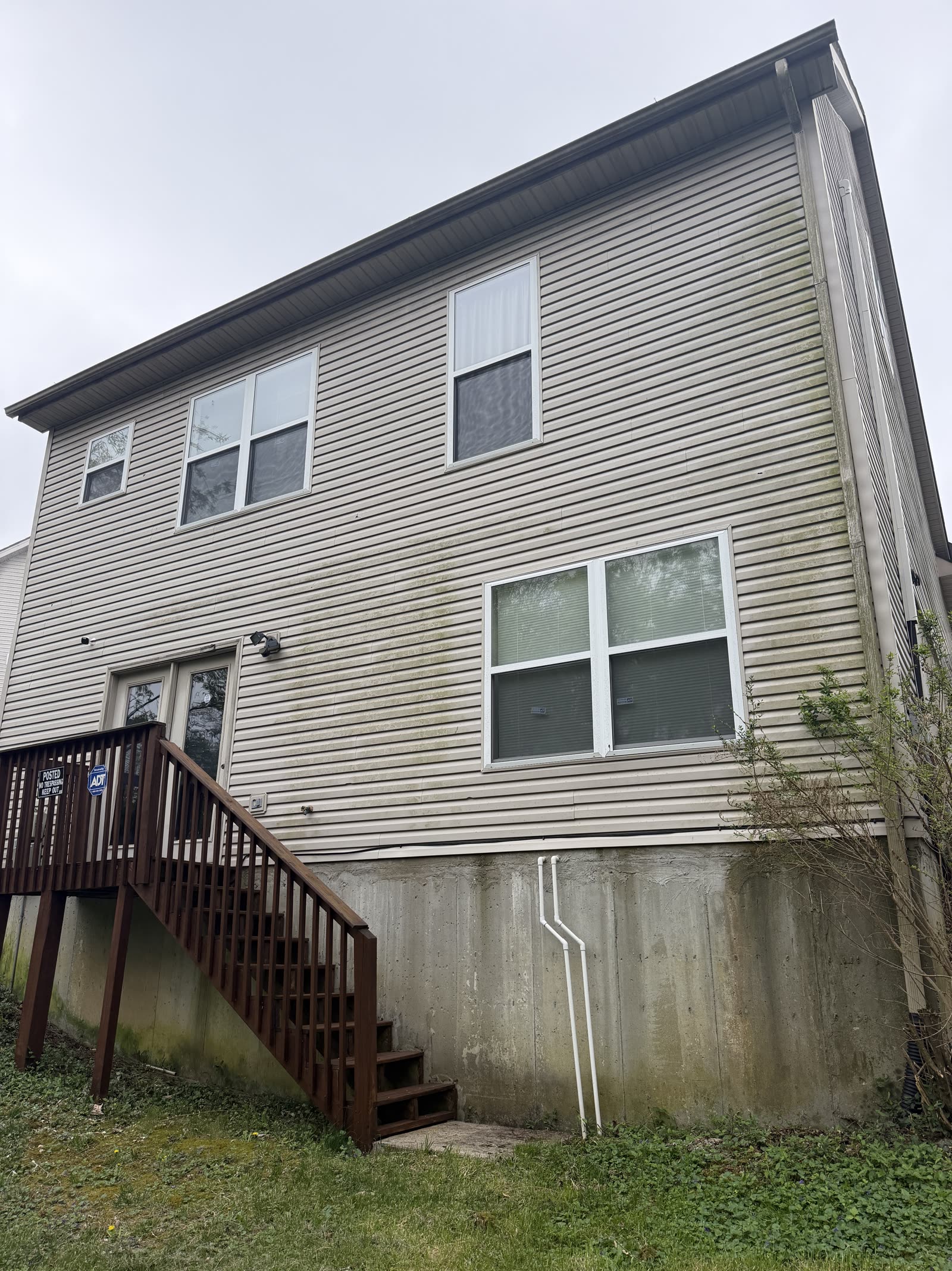 Two-story tan siding with green algae before pressure washing