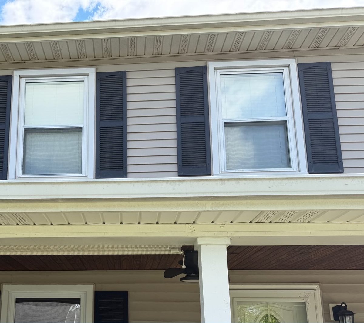 Tan vinyl siding with black shutters before soft washing